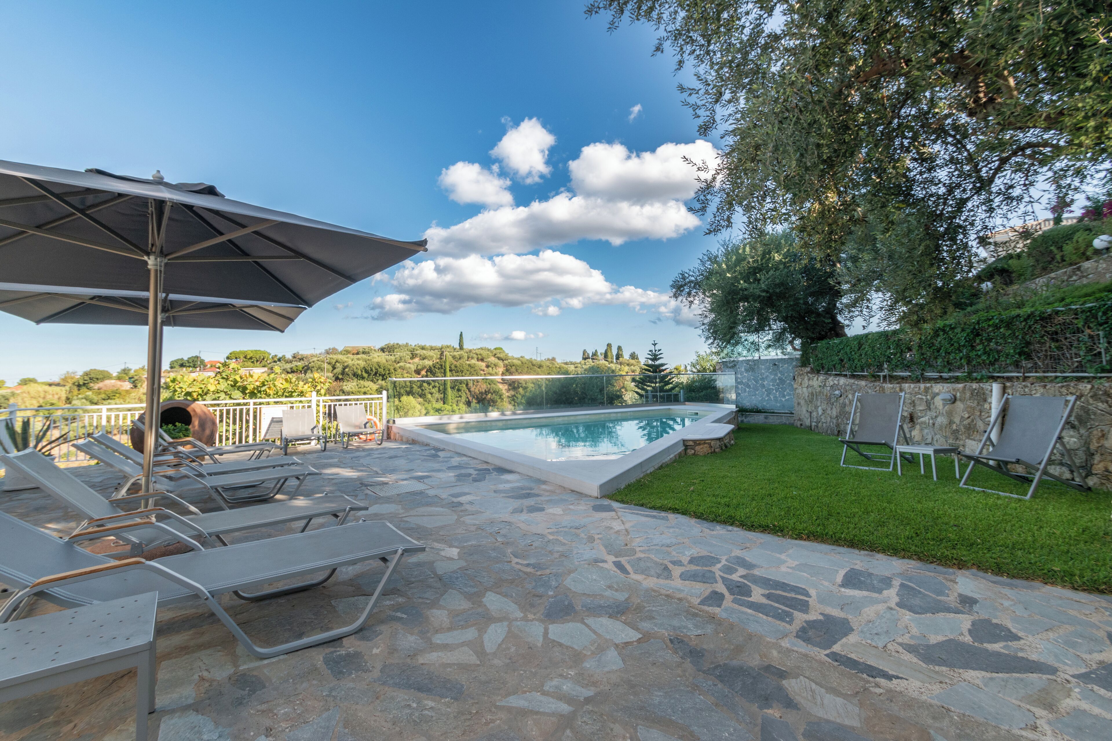 A stone patio with a swimming pool, lounge chairs, and an umbrella.