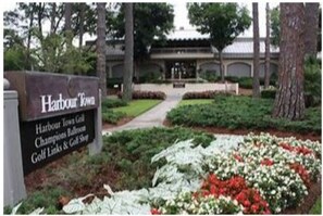 Harbour Town Golf Club features a beautifully maintained garden with a variety of flowers and shrubs, surrounded by a neatly trimmed hedge and a pathway leading to the entrance.