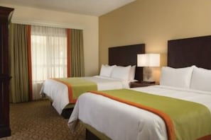Two single beds with white bedspreads and orange trim, a nightstand with a lamp, and a large window with sheer curtains.