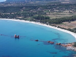 A coastal landscape with a beach, rocky outcrops, and a hilly terrain in the background.