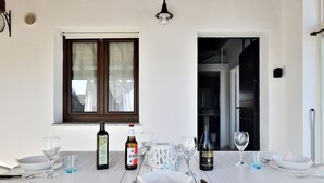 A dining table set with wine glasses, bottles, and plates in a room with white walls and a window. - Giorgio Holiday Home. Comfort and Relax for the Family, Just Steps from the Sea (Bari Sardo)