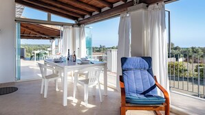 A balcony with a dining table set for two, a blue cushioned chair, and a view of the landscape. - Giorgio Holiday Home. Comfort and Relax for the Family, Just Steps from the Sea (Bari Sardo)