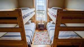 A room with two bunk beds, a small table, and a window with a view of the outdoors.