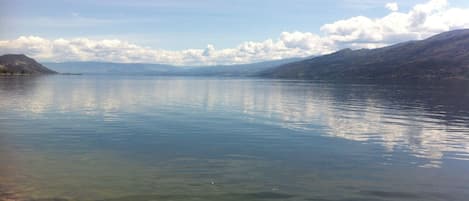 Un lago tranquilo con aguas cristalinas, rodeado de colinas y un cielo parcialmente nublado.