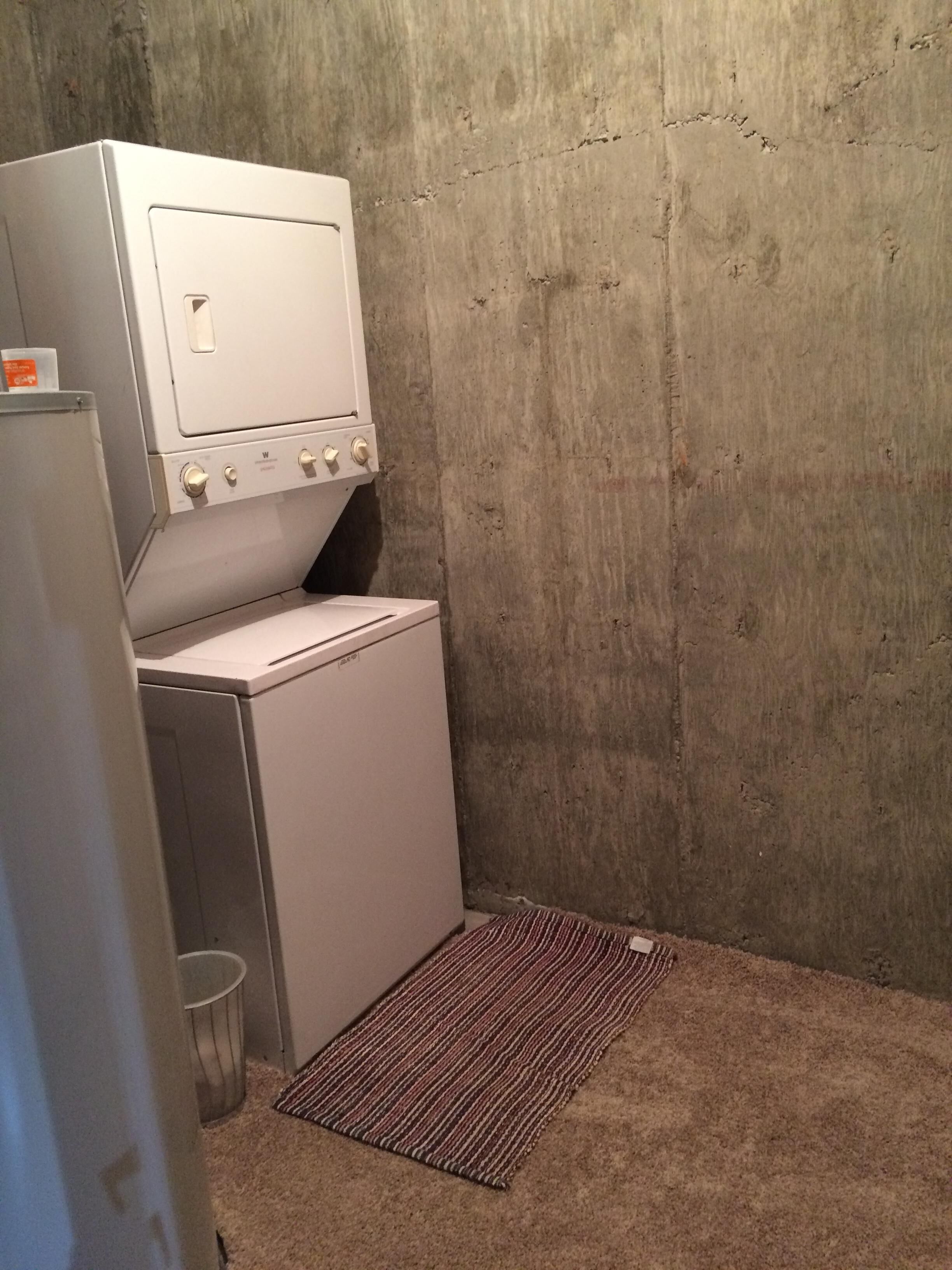 A compact laundry room with a washing machine and dryer, a metal trash can, and a striped rug on the floor.