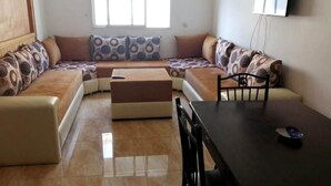 Una sala de estar con un juego de sofá, una mesa de comedor y un televisor montado en la pared.