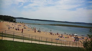 Una playa con gente tomando el sol y nadando, una torre de salvavidas y una vista del agua y las colinas al fondo.