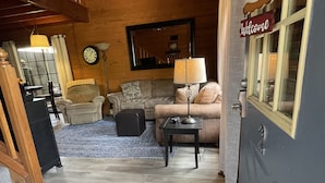 Una sala de estar acogedora con piso de madera, un sofá, una mesa de centro y una lámpara. Una escalera conduce a un nivel superior.