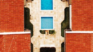 An aerial view of a swimming pool with a central water feature, surrounded by tiled walls and red-roofed buildings. - Manga Verde Beach 03: Pool and Beach view H (Pilar)