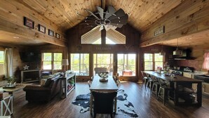 Una cabina spaziosa con soffitto alto, pareti in legno, un tavolo da pranzo centrale e un'ampia finestra con vista su una terrazza.