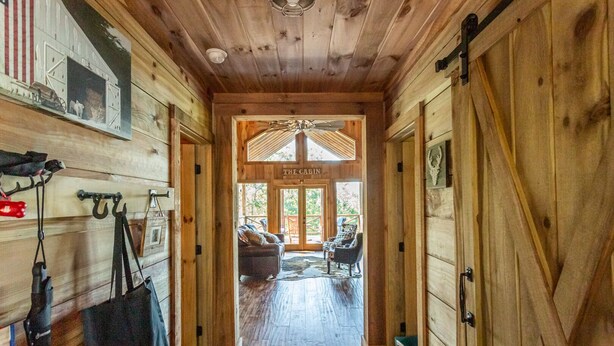 Interno di una baita in legno, con una porta centrale che recita 'The Cabin', che dà su un'area salotto esterna con due sedie.
