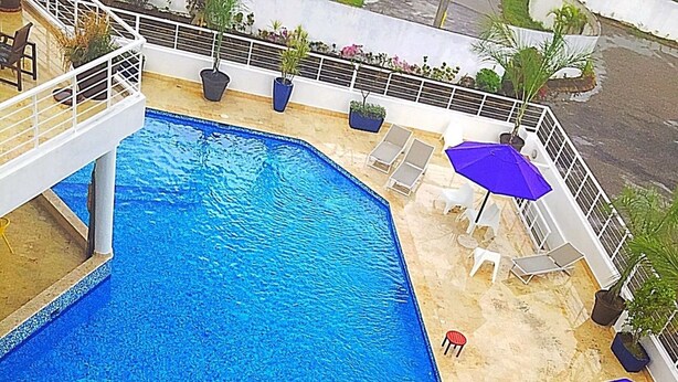 A rooftop pool area with a blue pool, white lounge chairs, and purple umbrellas.