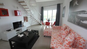 A modern living room with a black coffee table, a white sofa with a floral pattern, a TV on a white stand, and a staircase leading to an upper floor.