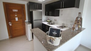 A compact kitchen with dark cabinets, a stainless steel refrigerator, a granite countertop, and a small sink.