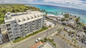 A multi-story hotel with balconies, a parking lot, and a view of the ocean.