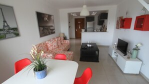 A modern living room with a white sofa, red chairs, a dining table, and a kitchen area in the background.