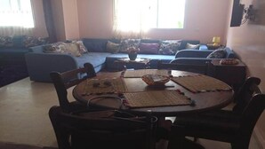 Uma sala de estar com um sofá, uma mesa de jantar com cadeiras e uma TV na parede.