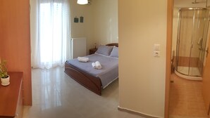 A bedroom with a bed, a bedside table with two potted plants, a shower, and a radiator.