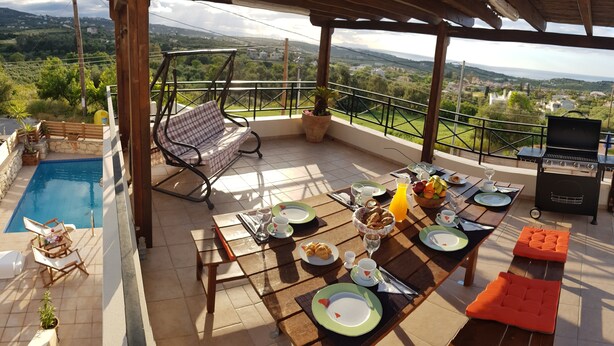 A terrace with a pool, dining setup, and a view of the countryside.