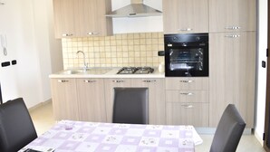 Uma cozinha moderna com armários de madeira clara, fogão a gás, forno e pia. Há uma mesa de jantar com cadeiras.