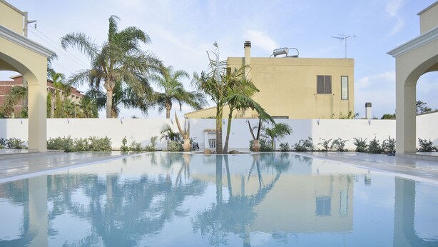 Piscina cercada por palmeiras e um edifício ao fundo.