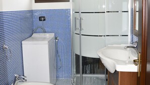 Casa de banho com duas sanitas, uma pia, um chuveiro e um tapete azul estampado.