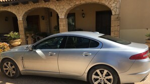 Um sedan prateado estacionado em frente a um edifício com arcos de pedra e um pátio com azulejos.