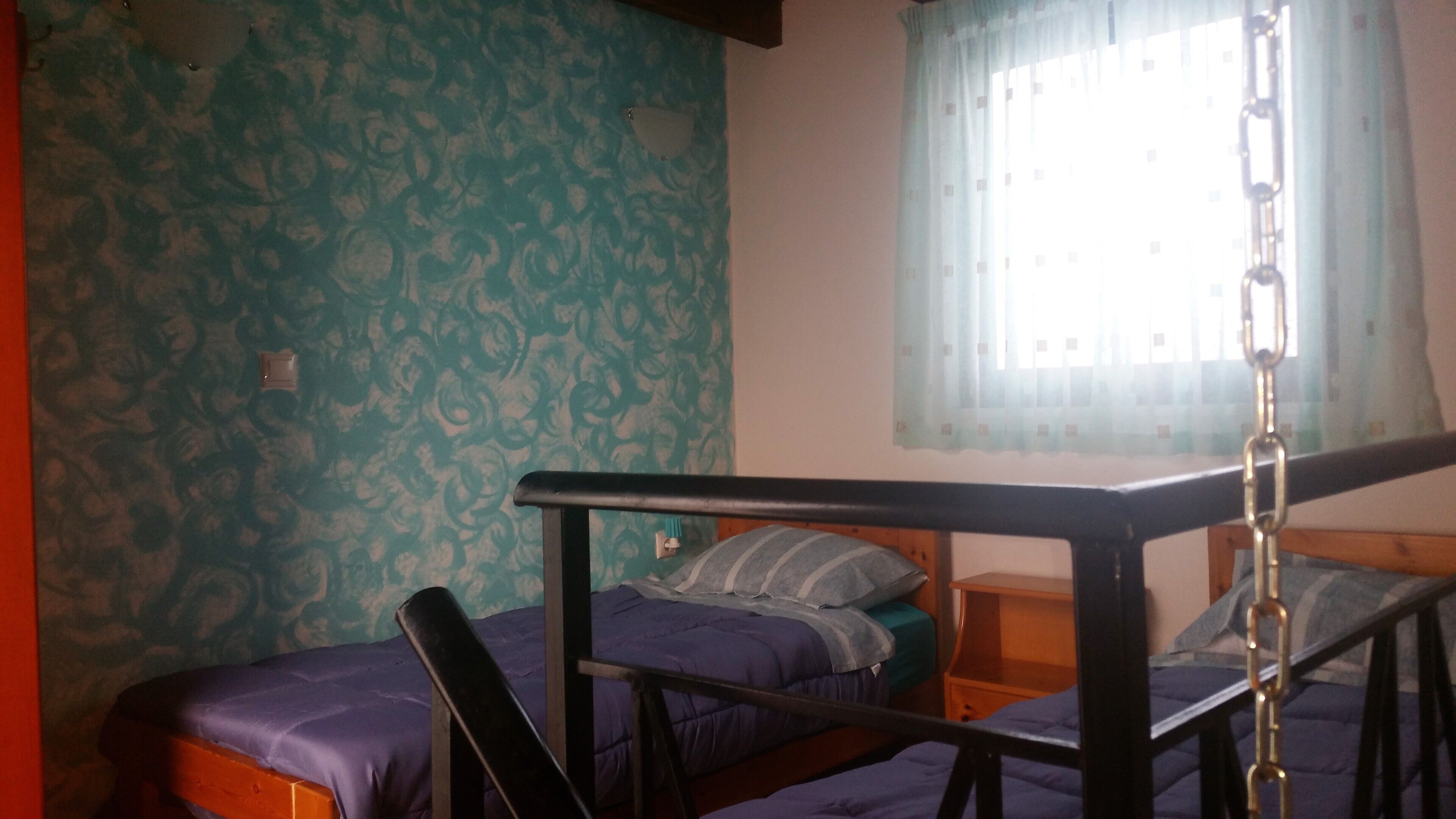 Een kamer met twee bedden, een raam met gordijn en een behang met patroon.