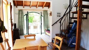 Un coin repas avec une table et des chaises en bois, un escalier orné d’un télescope, et une vue sur un espace extérieur aménagé en salon, accessible par une porte vitrée.