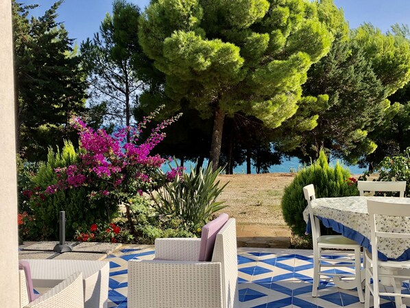 An outdoor seating area with a table and chairs, surrounded by lush greenery and a view of the sea.