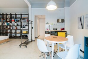 A modern apartment with a dining area, a kitchen, and a bookshelf.