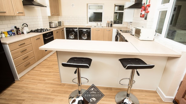 A modern kitchen with wooden cabinets, stainless steel appliances, and a central island with bar stools. - Celtic Bunkhouse Hostel (Merthyr Tydfil)