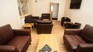 A furnished living room with leather sofas, a wooden coffee table, and a television mounted on the wall. - Celtic Bunkhouse Hostel (Merthyr Tydfil)