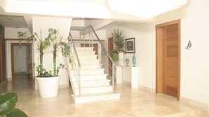 A staircase with a glass railing leading to a landing. There are potted plants on either side of the staircase.