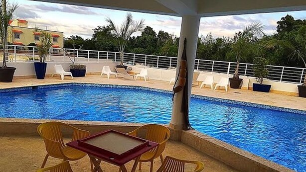 A pool area with a table and chairs, surrounded by potted plants and a railing.