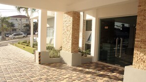 A hotel entrance with a tiled pavement, a glass door, and a stone pillar.