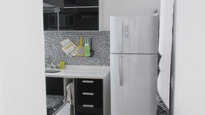 Une cuisine compacte équipée d’un réfrigérateur, d’un four à micro-ondes et d’un évier. Elle comprend un pare-feu en carrelage et un petit plan de travail avec des ustensiles de cuisine.