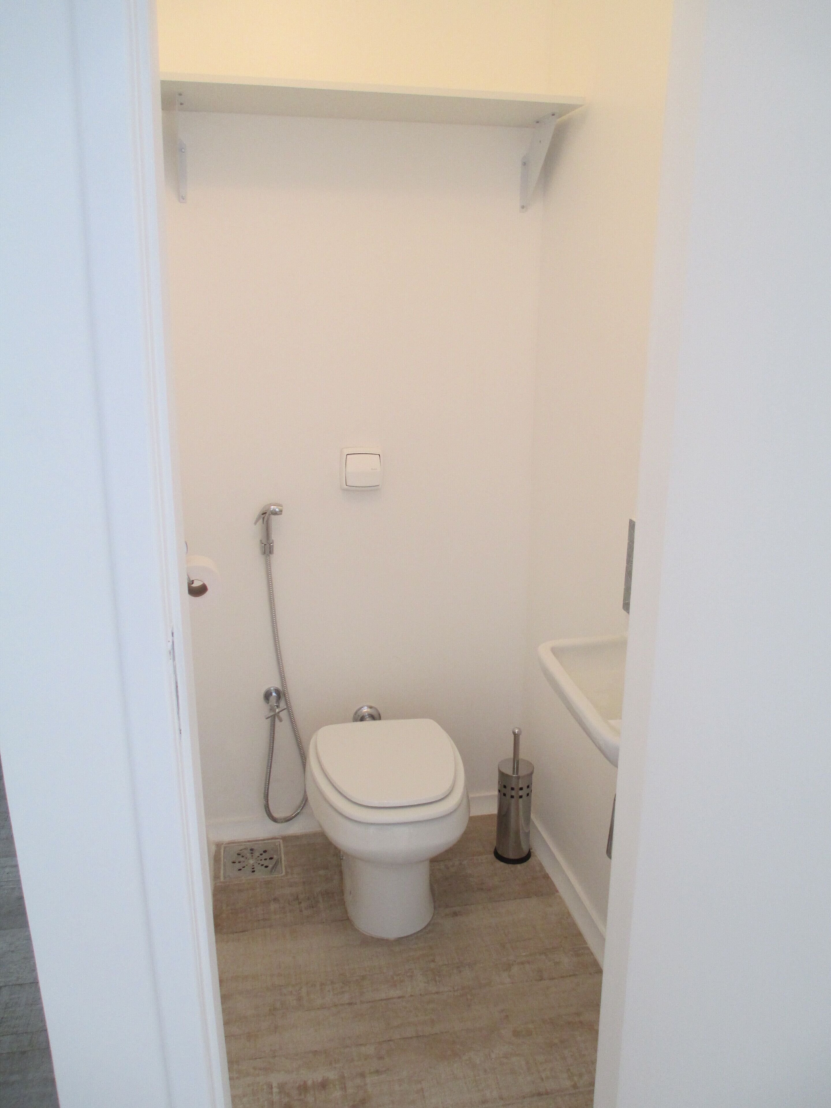 Une petite salle de bain blanche, équipée de toilettes, d’une douche et d’un lavabo.