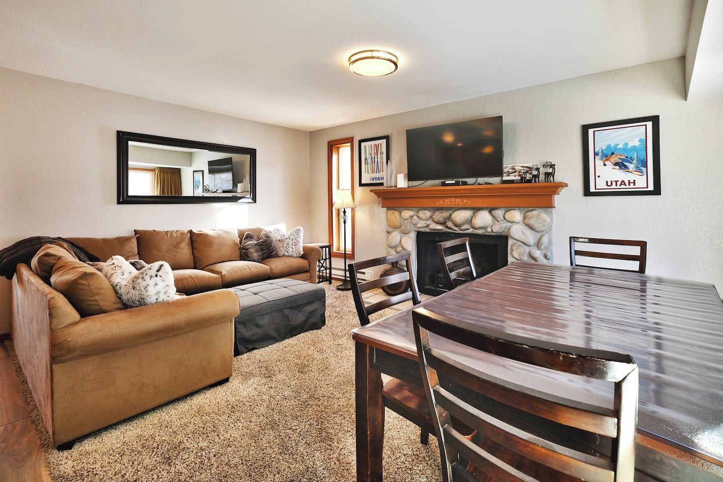 A living room with a sofa, a fireplace, a dining table, and a TV mounted on the wall.