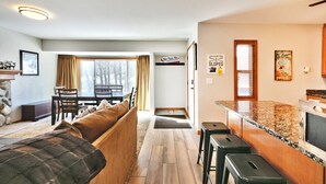 A cozy living room with a sofa, a dining table, and a kitchen area with a granite countertop and stools. - Canyons Mountain Views 2 br across from Resort (Park City)
