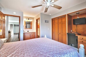 Ein Schlafzimmer mit Bett, Deckenventilator, Fernseher, Holzschränken und einem Badezimmer mit Spiegel und Waschbecken.