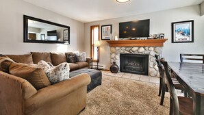 A living room with a stone fireplace, a television, and a dining area with a table and chairs. - Canyons Mountain Views 2 br across from Resort (Park City)