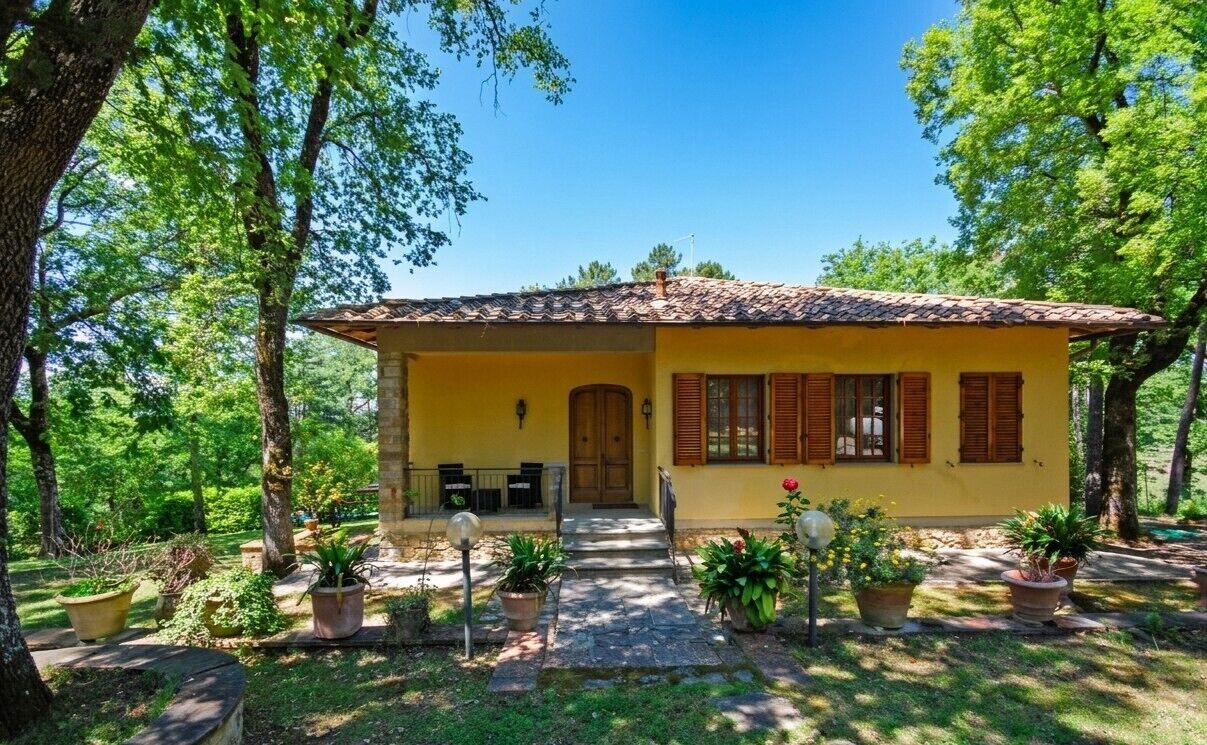 Une villa jaune, avec un toit recouvert de tuiles, entourée d’arbres et de plantes en pot.