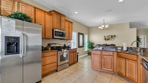 A modern kitchen with wooden cabinets, stainless steel appliances, a granite countertop, and a central island. - LUXE DISNEY HOME, POOL W/ SPA, GAME ROOM,  FREE NETFLIX & WIFI  (Davenport)