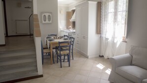 Una cocina con armarios blancos, una mesa de comedor con sillas y una ventana con cortinas translúcidas.