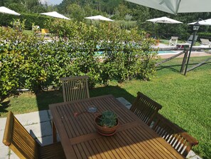 Un tavolo in legno con sedie e una pianta in vaso, circondato da una piscina e ombrelloni.