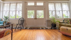Una habitación con piso de madera, una puerta blanca con paneles de vidrio, una silla negra, un sillón azul, un sofá verde y una planta en maceta.