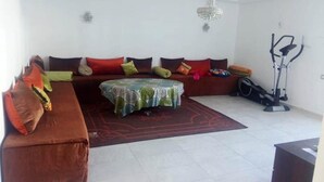 Una sala de estar con un sofá marrón, una mesita con mantel estampado, una bicicleta estática y un candelabro.