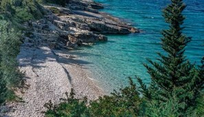 A rocky coastline with clear turquoise water and a pebble beach.