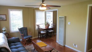 A living room with a sofa, a dining table with chairs, a ceiling fan, and a window with blinds.